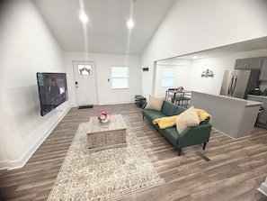 A living room with a green sofa, a coffee table with flowers, a TV, and a kitchen area with a refrigerator. - Enjoyable 4-bedroom house with AC in charming Atlanta (Atlanta)