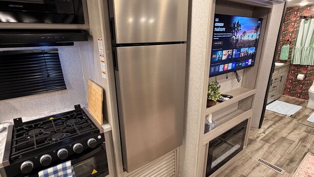 Uma cozinha moderna com eletrodomésticos de aço inoxidável, fogão a gás e uma TV de tela plana instalada acima do forno.