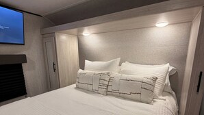 Quarto com cama grande, cabeceira com iluminação embutida, televisão na parede e guarda-roupa.