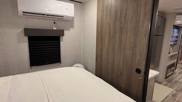 Habitación de hotel con cama, unidad de aire acondicionado, armario de madera y baño con inodoro y lavamanos.