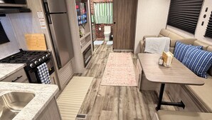 Cozinha compacta de RV, com fogão, pia, refrigerador e área de jantar com mesa e cadeiras.