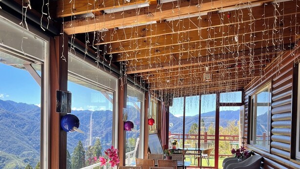 Un amplio comedor al aire libre con vigas de madera y luces colgantes, con vistas a un paisaje montañoso.