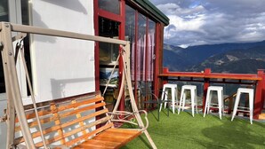 Un balcón con una hamaca de madera, taburetes de bar blancos y vistas a las montañas.