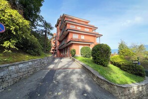 A multi-story building with a stone wall entrance, a paved driveway, and well-maintained greenery. - Manuela's Apartment Stresa next to center Lake View Terrace, Stresa, Italy (Stresa)