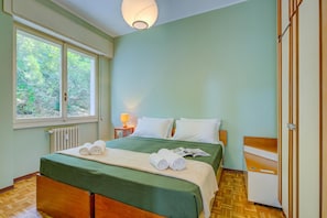 A hotel room with a bed, a window, a radiator, and a bedside table with a lamp. - Manuela's Apartment Stresa next to center Lake View Terrace, Stresa, Italy (Stresa)