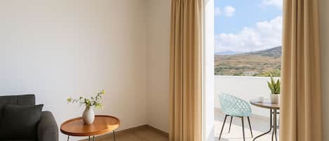 Una habitación moderna con sofá, una mesita de madera con un florero, y un balcón con una silla y una mesa.