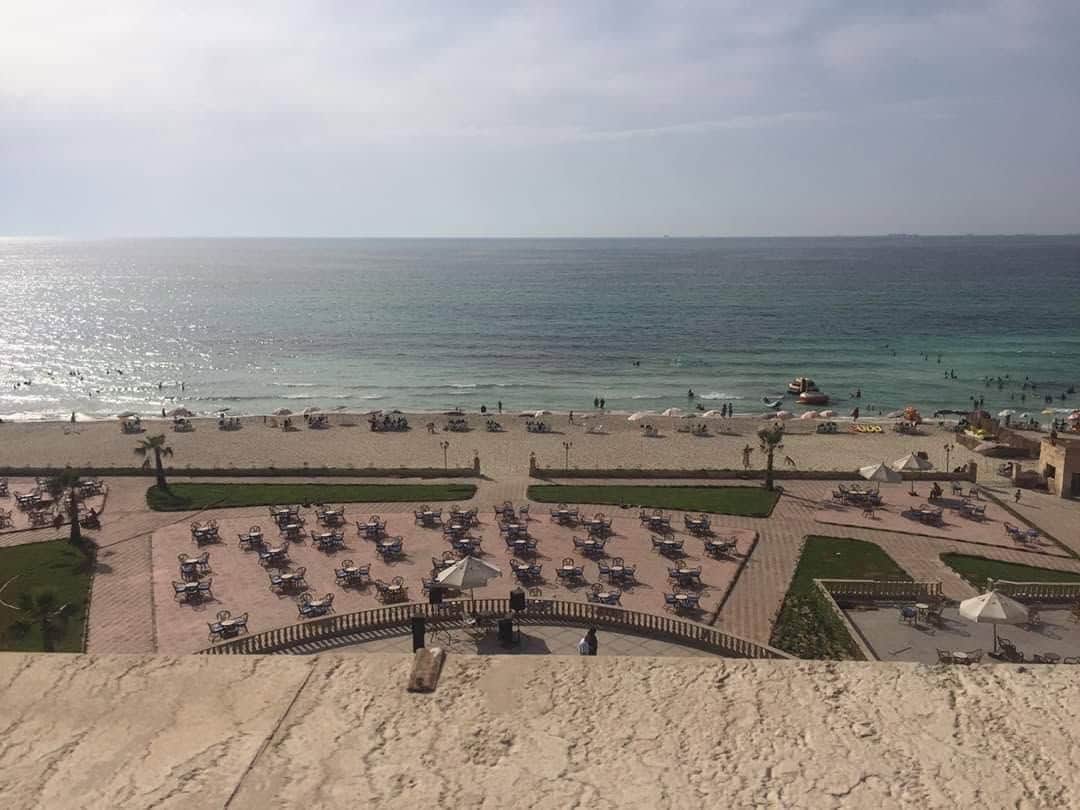 A beach with a paved area, umbrellas, and chairs.