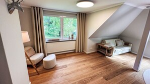 A cozy room with a wooden floor, a sofa, a small table, and a window with curtains. - The OAK SUITE by Interhome (Bad Bederkesa)