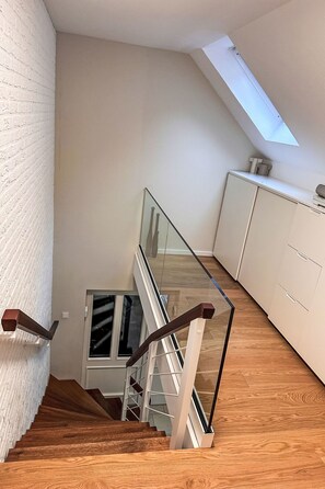 Un escalier moderne avec des rampes en verre, des marches en bois et une verrière.