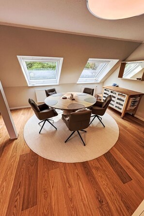 A room with a round table, four chairs, a radiator, a wooden cabinet, and two skylights. - The OAK SUITE by Interhome (Bad Bederkesa)
