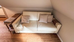 A corner room with a white leather sofa, two pillows, a wooden side table, and a book titled 'GÄSIE'. - The OAK SUITE by Interhome (Bad Bederkesa)