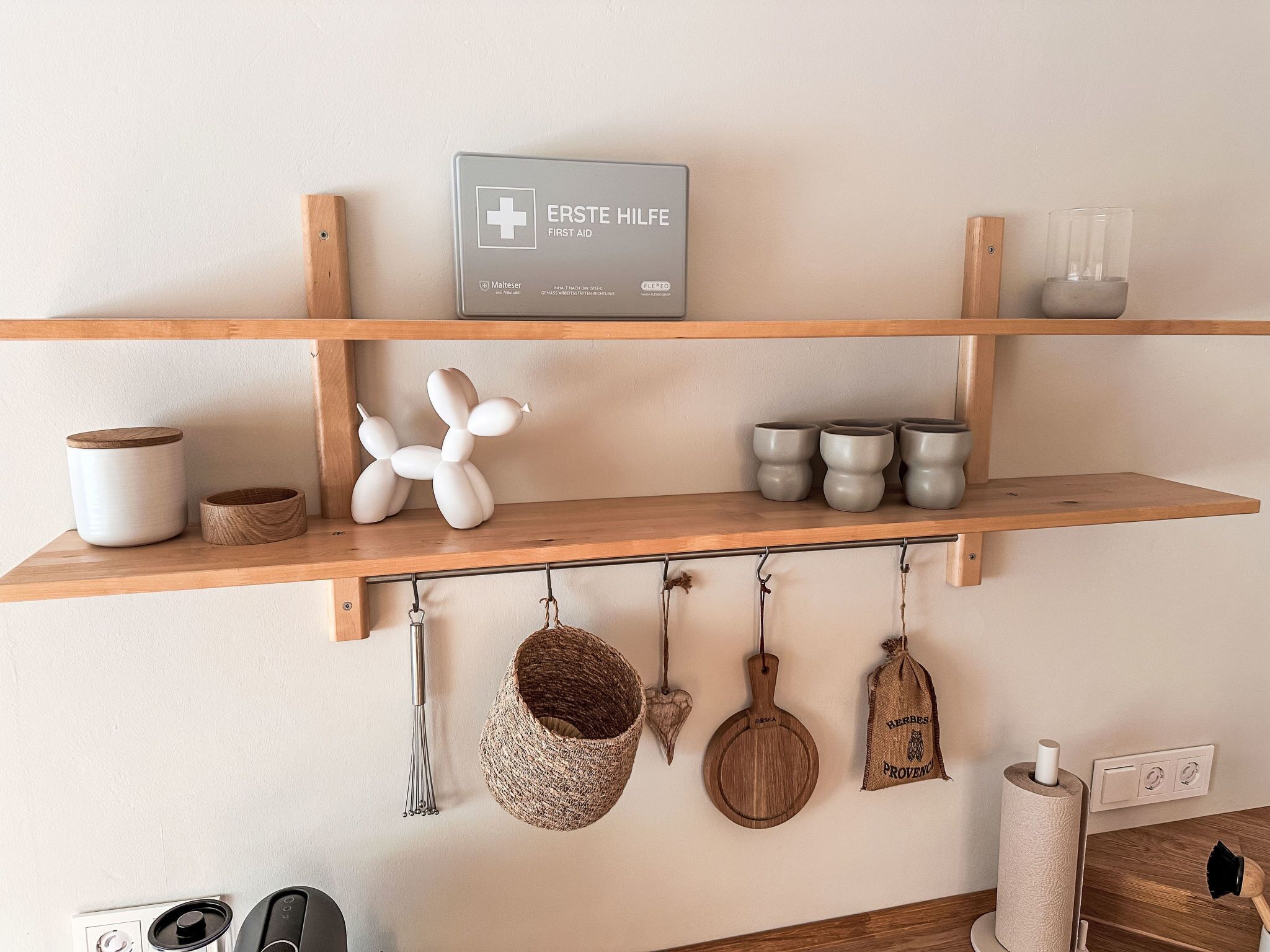 A kitchen with wooden shelves, a first aid sign, kitchen utensils, and a hanging pot rack.