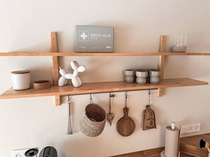 A kitchen with wooden shelves, a first aid sign, kitchen utensils, and a hanging pot rack. - The OAK SUITE by Interhome (Bad Bederkesa)