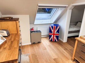 Une petite pièce dotée d’une lucarne, d’un coin cuisine, d’un lit et d’un meuble de rangement orné d’un drapeau Union Jack.
