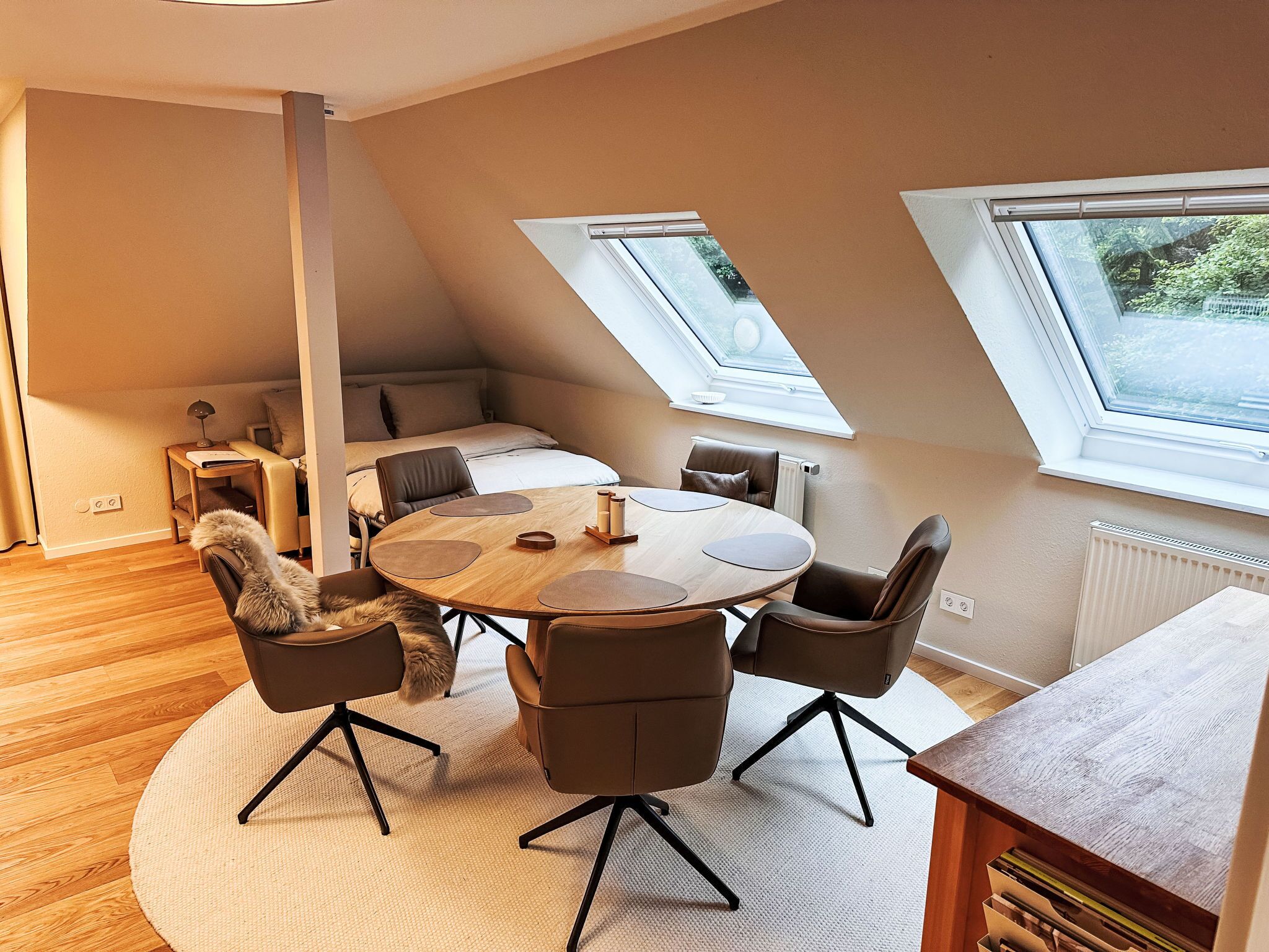 Een moderne loft slaapkamer met een schuine kap, een ronde houten eettafel en twee dakramen.