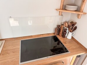 A kitchen with a wooden countertop, a black induction cooktop, and wooden utensils. - The OAK SUITE by Interhome (Bad Bederkesa)