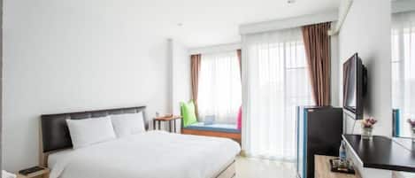 Habitación de hotel con cama, escritorio, televisión y ventana con cortinas.