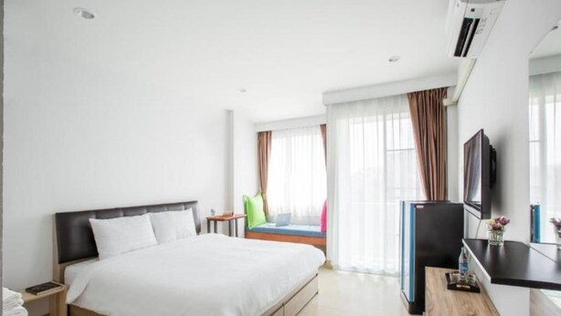 Habitación de hotel con cama, escritorio, televisión y ventana con cortinas.