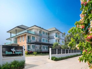 A multi-story hotel with a gated entrance, a signboard, and a well-maintained garden. - Baan I Inspire (Phrae)