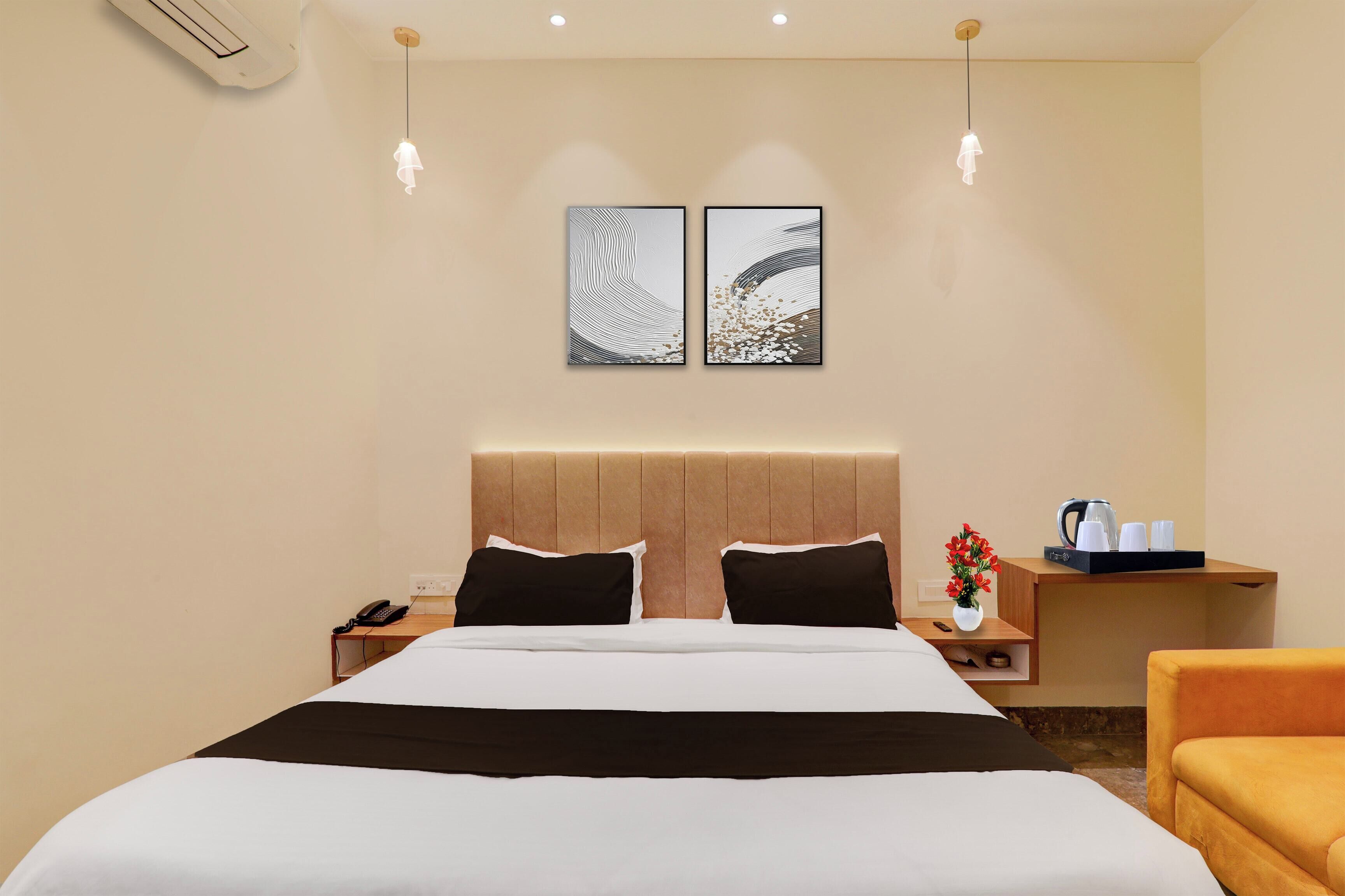A hotel room with a bed, bedside tables, a nightstand, a vase with flowers, a coffee maker, and two wall art pieces.