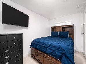 A bedroom with a bed, a dresser, and a television mounted on the wall. - Coastal Chic Retreat | Steps to the Sand (Newport Beach)