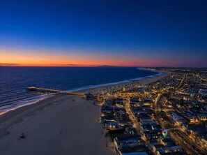 Eine Küstenstadt im Abendlicht mit einer langen Mole, die sich ins Meer erstreckt, einem Strand und dicht bebauten Stadtgebäuden mit Straßen und Häusern.