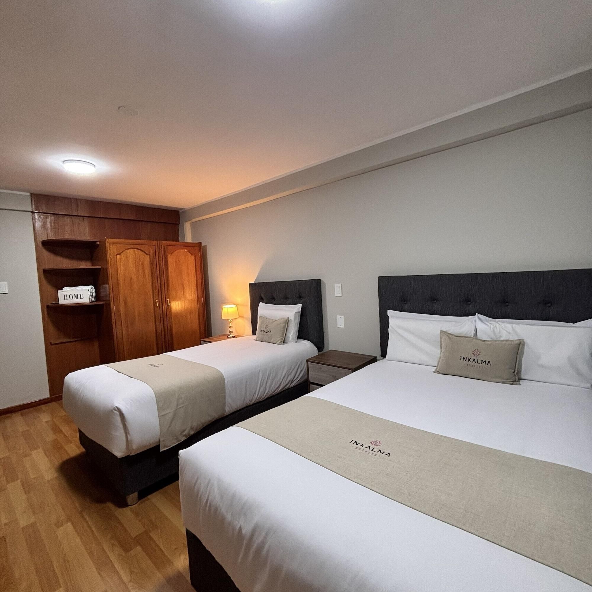 A hotel room with two beds, a wardrobe, and a nightstand with a lamp.