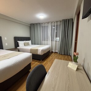 A hotel room with two beds, a desk, a chair, a small table with a card, and a potted plant. - Inkalma Centro (Arequipa)