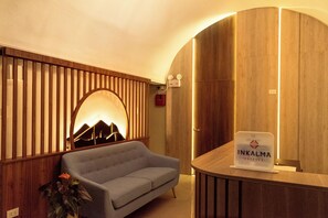 A hotel reception area with a sofa, a wooden panel wall with a mountain design, and a reception desk with a sign. - Inkalma Centro (Arequipa)