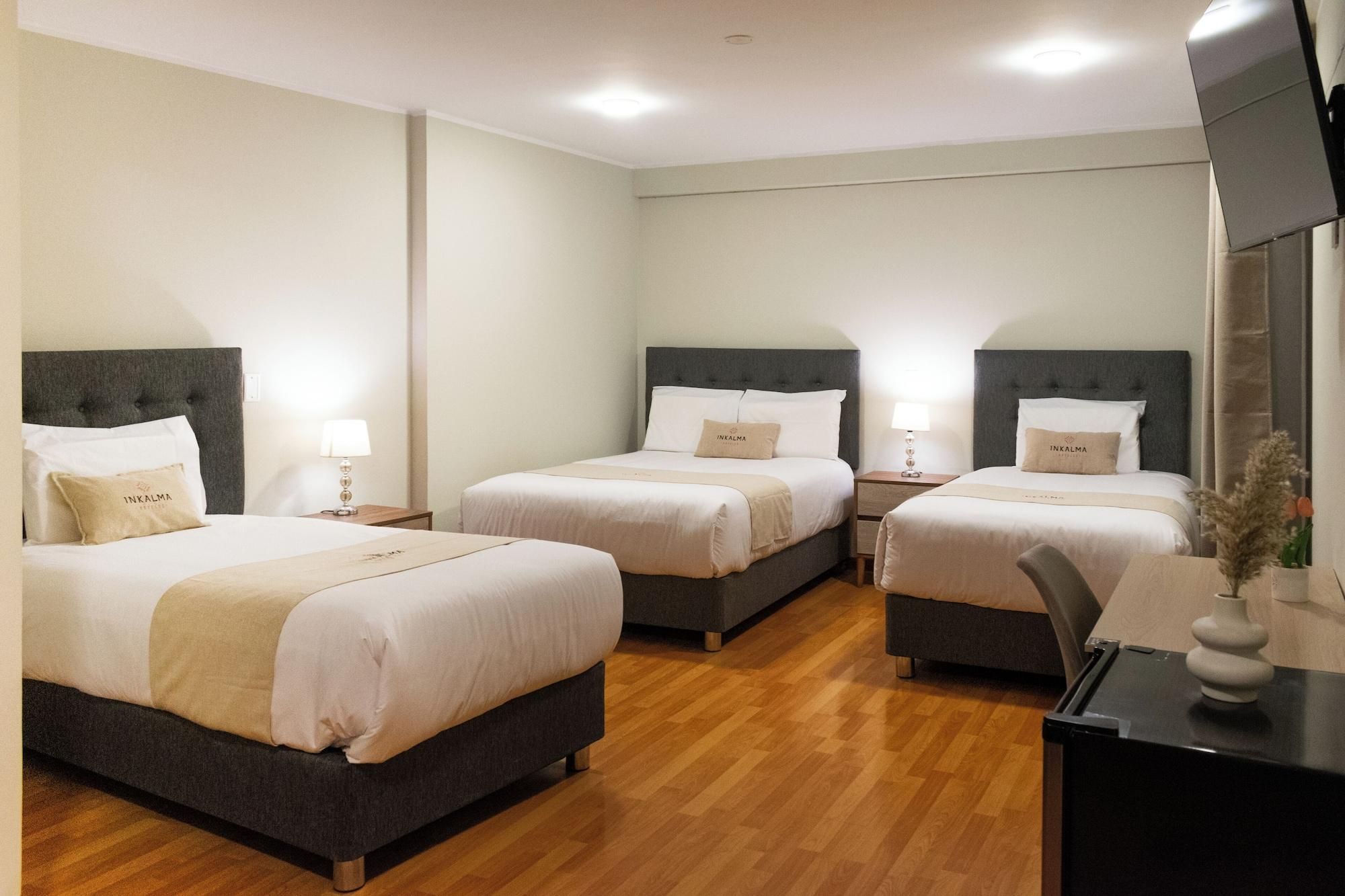 Habitación de hotel con tres camas, cada una con cabecero y mesitas de noche.