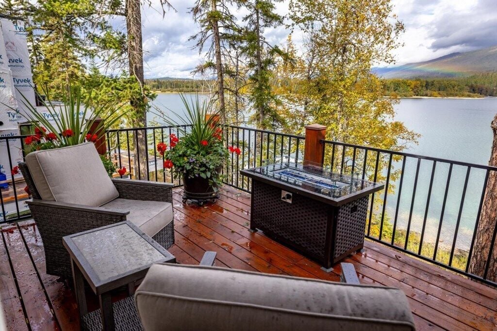 A wooden deck with outdoor furniture, a fire feature, and a view of a lake and forest.