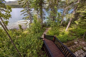 A wooden bridge leading to a dock over a lake surrounded by dense forest. - Whitefish Lake Waterfront Retreat W/ Private Dock (Whitefish)