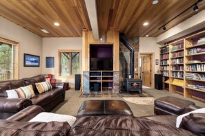 A cozy living room with a fireplace, leather sofas, a bookshelf, and a stone fireplace surround. - Whitefish Lake Waterfront Retreat W/ Private Dock (Whitefish)
