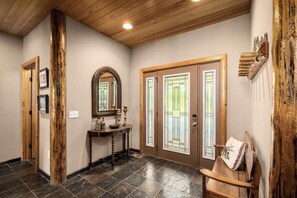 A hallway with a wooden door, a mirror, and a console table with decorative items. - Whitefish Lake Waterfront Retreat W/ Private Dock (Whitefish)