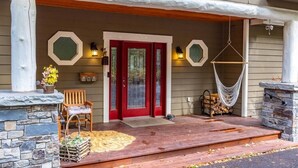 A house with a red door, a porch with a stone fireplace, and a hammock. - Whitefish Lake Waterfront Retreat W/ Private Dock (Whitefish)