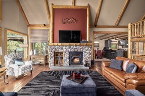 Ein gemütliches Wohnzimmer mit Kamin aus Stein, Holzbalken, einem Ledersofa und einem Fernseher über dem Kamin.
