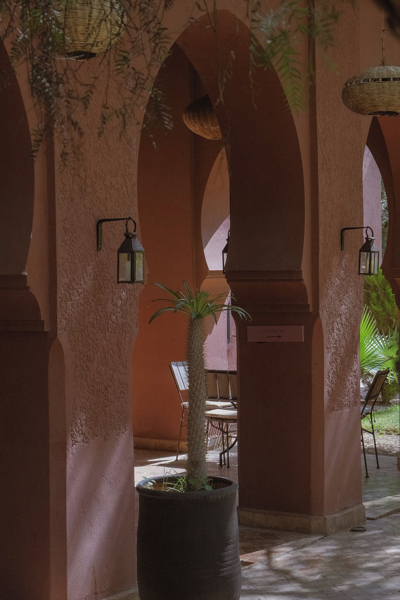 An indoor courtyard with arches, potted plants, and a sign indicating a pool.