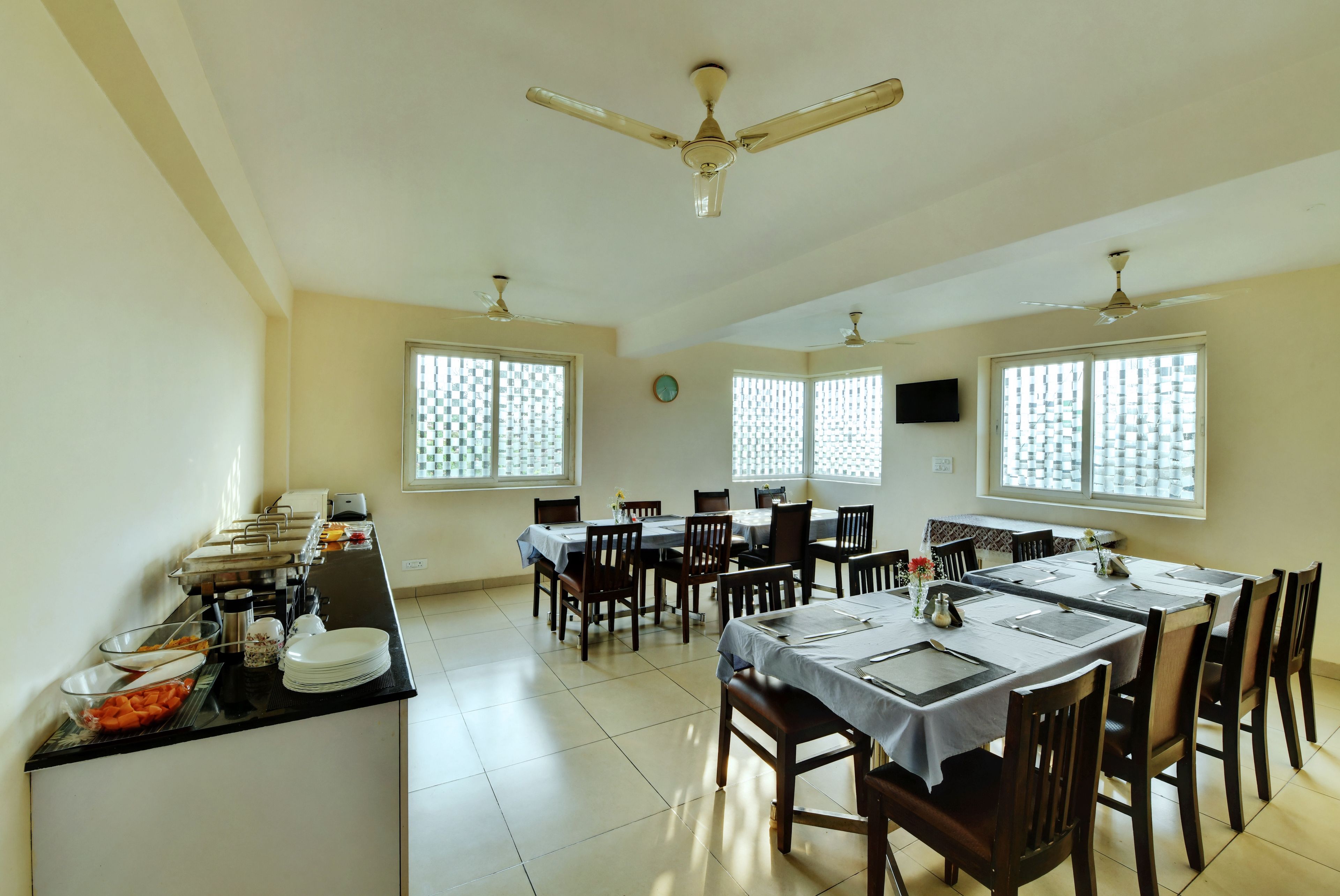 A dining area with multiple tables and chairs, a buffet counter with food items, and ceiling fans.