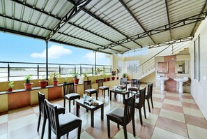 Un área de estar al aire libre cubierta con mesas y sillas, plantas en macetas y vistas de la ciudad.