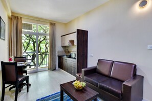 A living room with a sofa, a dining table with chairs, a kitchen area, and a balcony with curtains. - Avm Comfort Inn (Bengaluru)