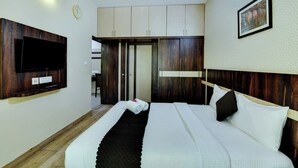 A hotel room with a bed, a flat-screen TV mounted on the wall, a ceiling fan, and a clock. - Avm Comfort Inn (Bengaluru)