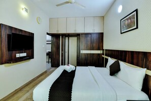 A hotel room with a bed, a flat-screen TV mounted on the wall, a ceiling fan, and a clock. - Avm Comfort Inn (Bengaluru)