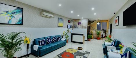 A reception area with a blue sofa, a reception desk, potted plants, and artwork on the walls.