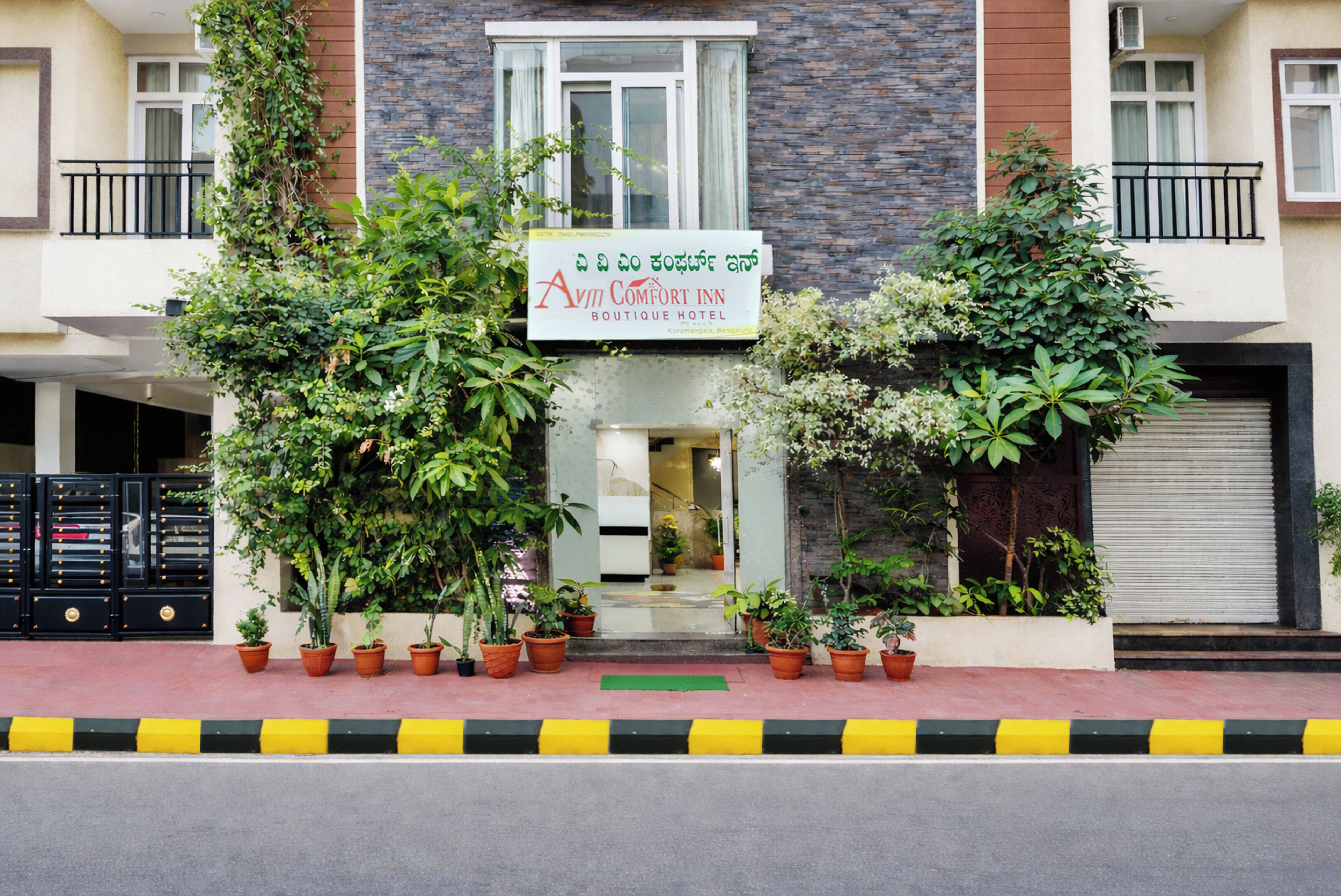 A hotel entrance with a signboard, potted plants, and a gated driveway.