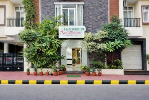 Entrada de hotel con letrero, plantas en macetas y un camino de acceso porticado.