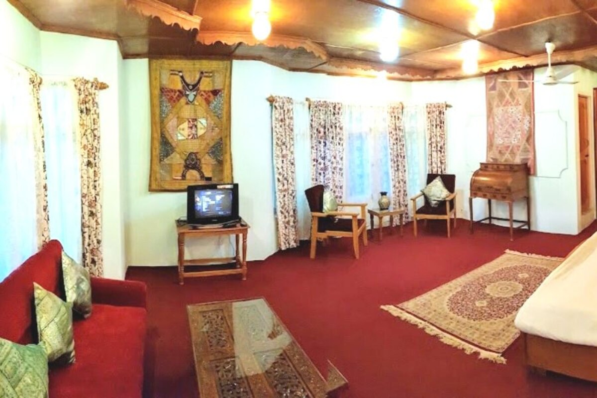 A hotel room with a large bed, a television, a wooden wardrobe, and a red sofa.
