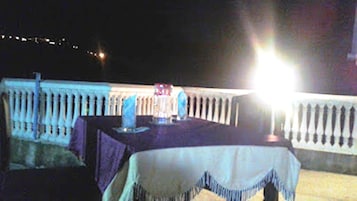 An outdoor dining area with tables and chairs, a railing, and a view of the night sky.