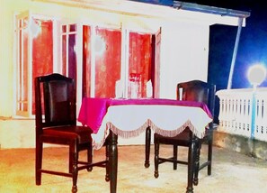 Uma área de refeições ao ar livre com uma mesa coberta por toalha branca e duas cadeiras.