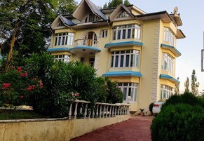 Un edificio de varios pisos con balcones, un sendero rojo y follaje circundante.