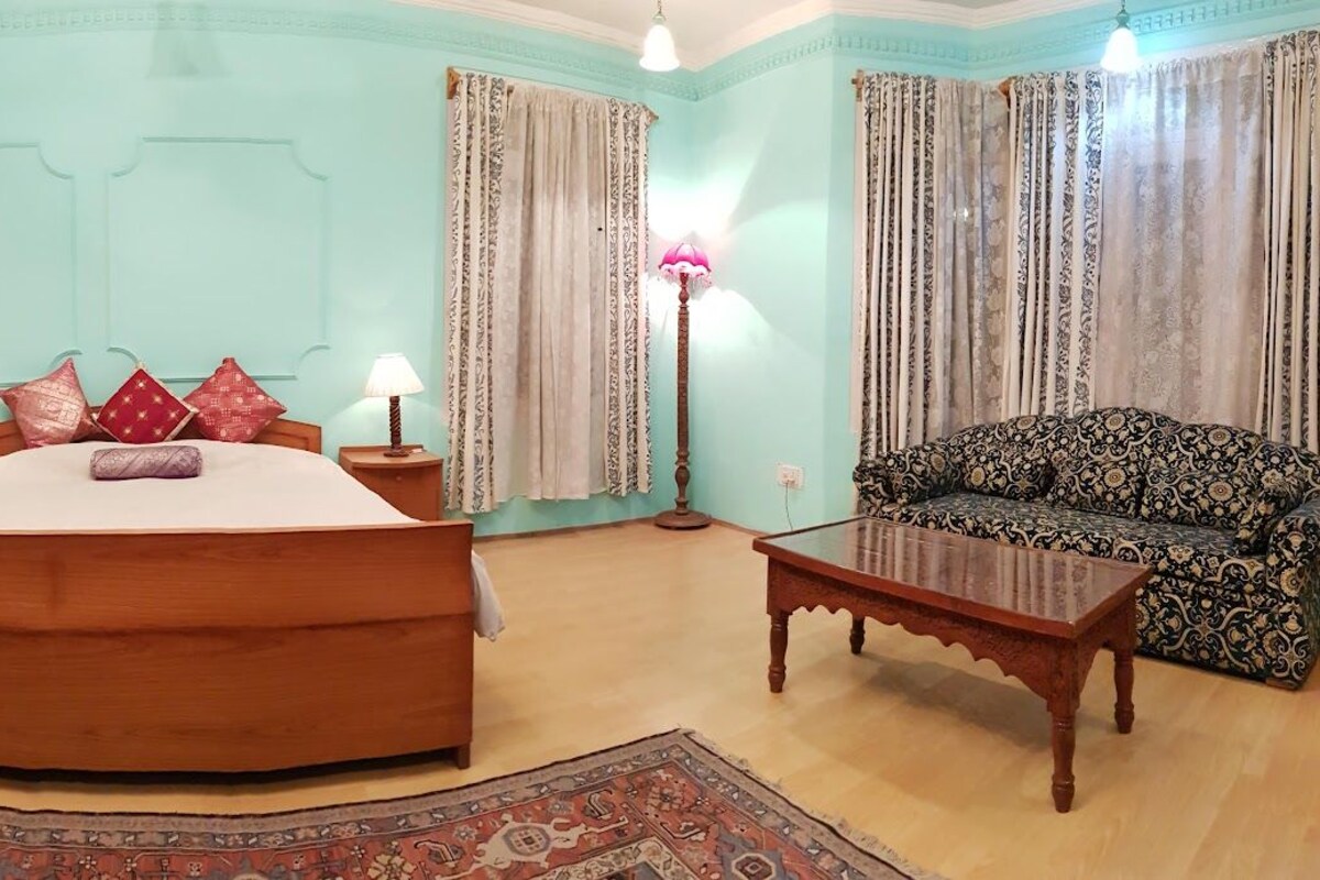 A bedroom with a large bed, a wooden wardrobe, a patterned sofa, and a floor lamp.